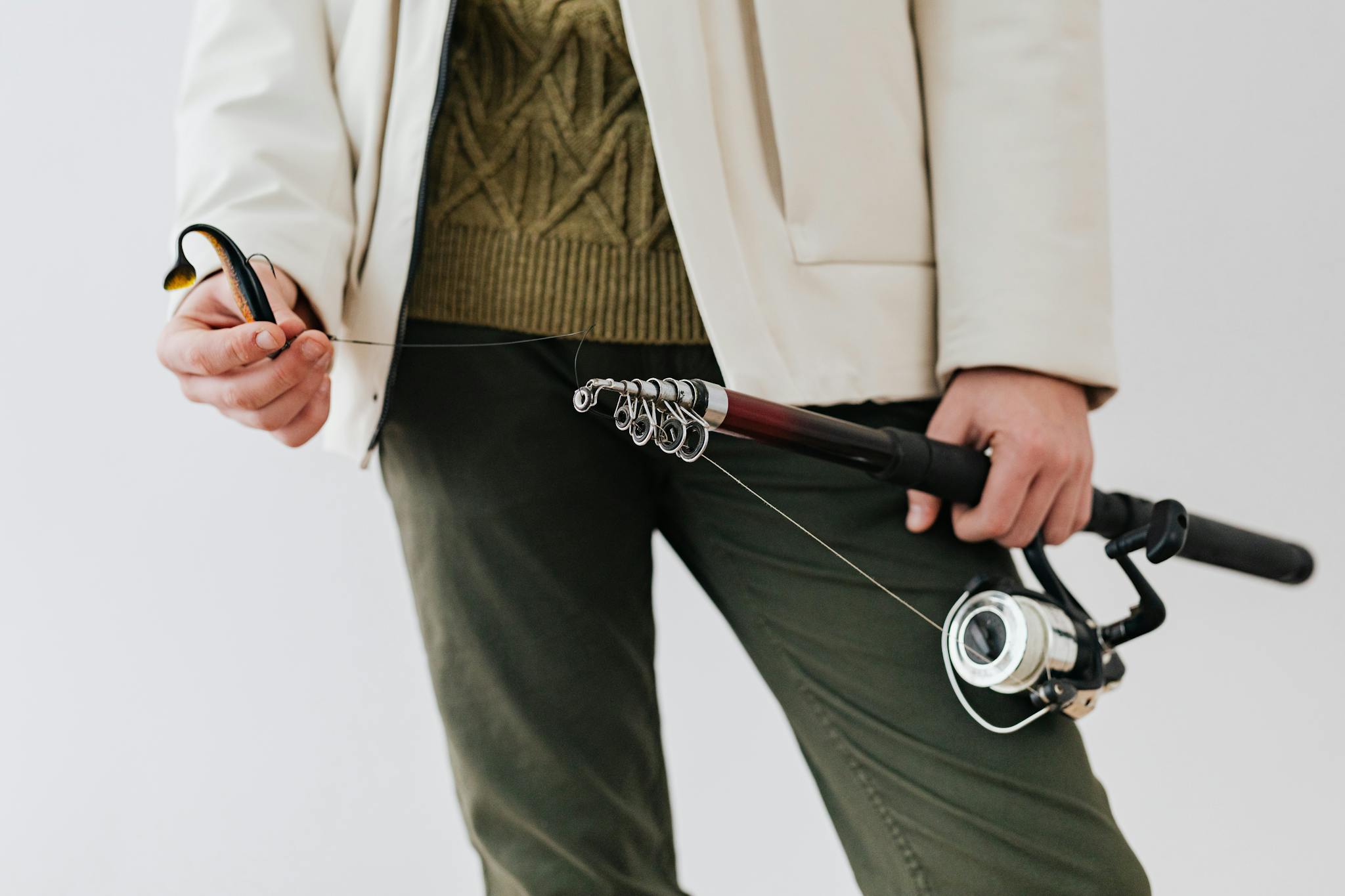 A person in outdoor attire holding a fishing rod with bait, showcasing fishing equipment details.