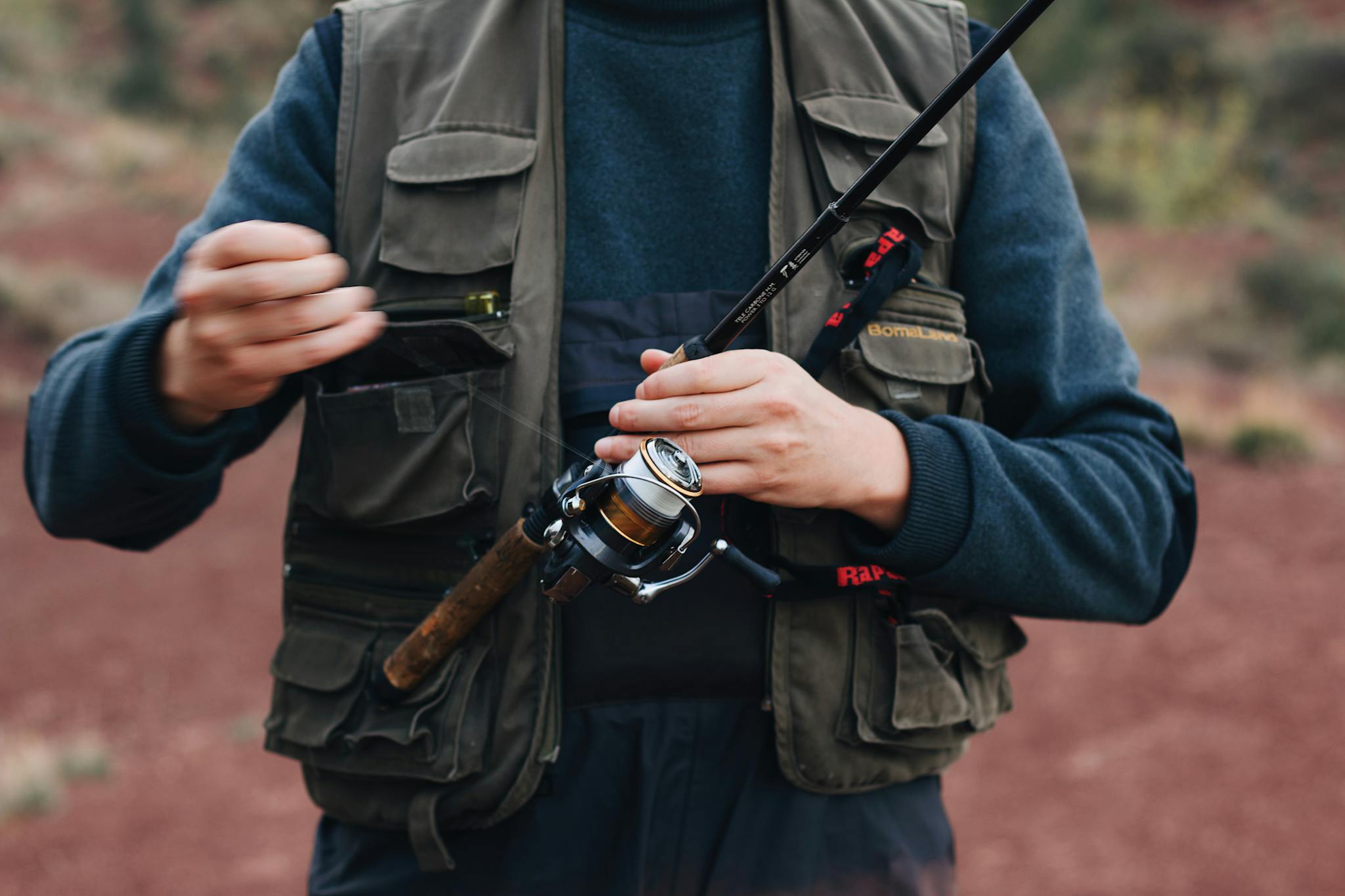 Close-up of a man holding a fishing rod, adjusting the line outdoors.